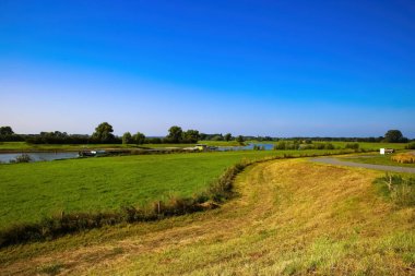 Hollanda Bronkhorst ve Zutphen arasındaki mavi yaz gökyüzüne karşı tarımsal tarlaları ve Ijssel nehri olan tipik Hollanda kırsal alanındaki bisiklet pistinden bir görüntü