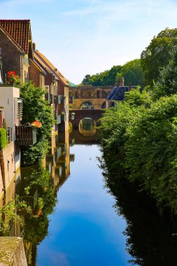 14. yüzyıldan kalma ev ve ağaçlarla dolu su kanalı üzerinde mavi yaz gökyüzüne karşı yansıyan ortaçağ su kapısı taşından duvarına bakın - Zutphen (Berkelpoort), Hollanda