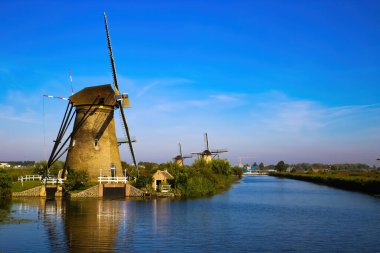 Hollanda 'nın kırsal kesimindeki Kinderdijk, Hollanda' daki derin mavi bulutsuz yaz gökyüzüne karşı yeşil çayır üzerindeki eski yel değirmenleri üzerindeki Hollanda su kanalına bakın.