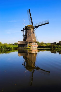 Hollanda 'nın kırsal kesimindeki Kinderdijk, Hollanda' da derin mavi bulutsuz yaz gökyüzüne bakan eski bir yel değirmeninin yansımasıyla Hollanda su kanalına bakın.
