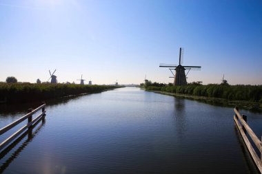 Ufuktaki Hollanda su kanalı üzerinde sabah güneşinde kırsal alanda rüzgar değirmenleri ve baş döndürücü mavi gökyüzü - Kinderdijk, Hollanda