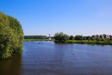 Alblas nehrinin yeşil ağaçları, konut evleri ve mavi yaz gökyüzüne karşı yel değirmeni - Alblasserdam, Hollanda