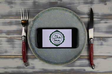 Viersen, Almanya - 9 Haziran. 2021: Tabakta çatal bıçakla birlikte helal sertifika servislerinin logosu olan akıllı telefonun kapatılması (merkeze odaklan)