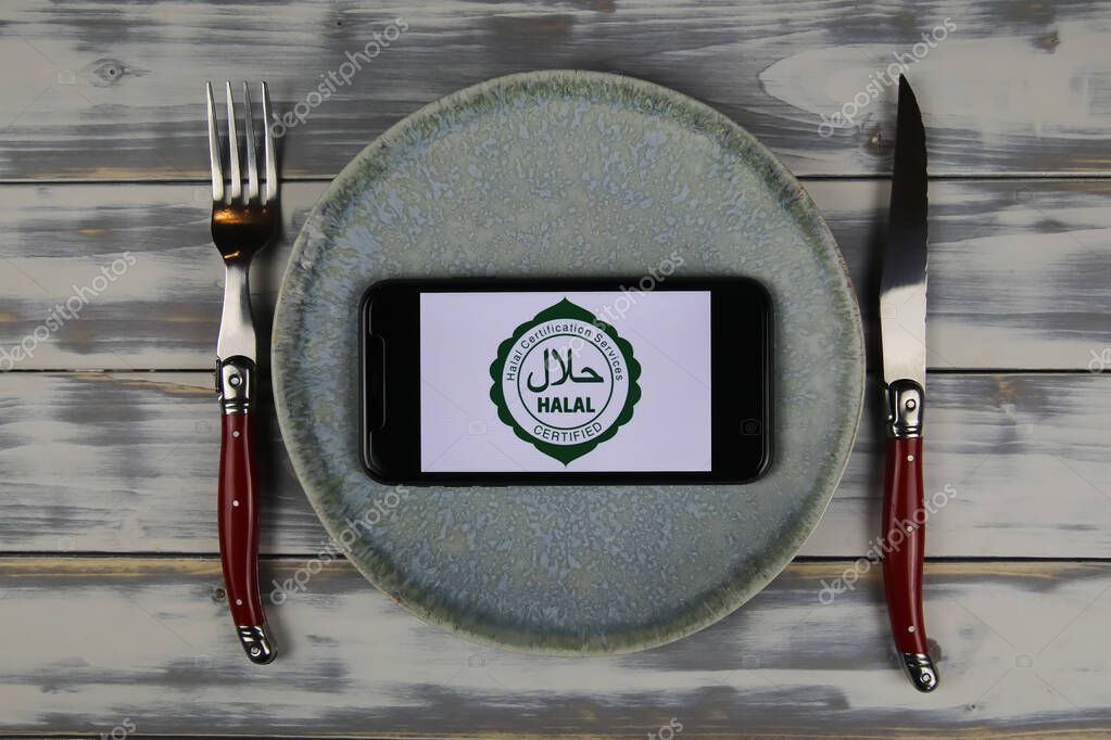Viersen, Germany - June 9. 2021: Closeup of smartphone with logo lettering of halal certification services on plate with cutlery (focus on center)