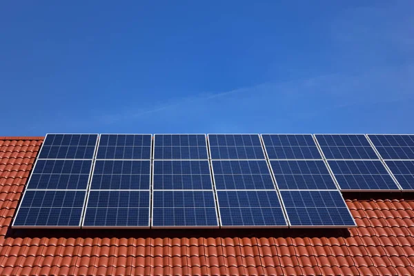 Mavi gökyüzüne bağlı güneş panelleri olan kırmızı kiremitleri kapat