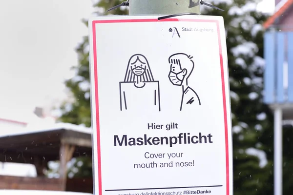2021年8月1日ドイツのアウクスブルクでは 感染の危険性がある場合はマスクが必要であることを英語で知らせるランプポストにプラスチックサインが掛けられています — ストック写真