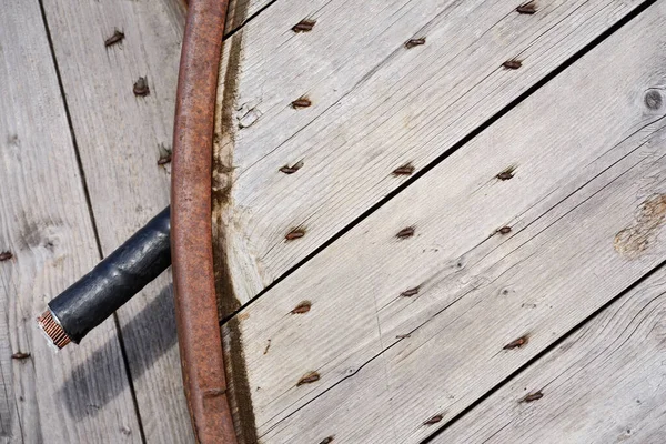 Close up, texture and background of a cable drum made of weathered wood, with several screws and rusty metal parts. A piece of cable hangs on the side