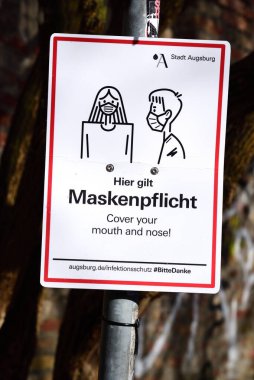 Augsburg 'da, dışarıda maske takmanın zorunlu olduğunu belirten bir direğe bir tabela asılır. Bu Almanca ve İngilizce.