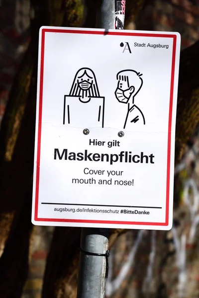 アウクスブルクでは 屋外でマスクを着用することが義務付けられていると述べている極にサインが取り付けられています これはドイツ語と英語で — ストック写真