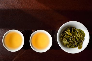 Durgun bir hayat ve iki Çin çay fincanı üzerinde altın çay ve taze yeşil çay yapraklı bir çaydanlık, kahverengi bir masada yan yana.