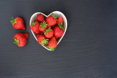 Yanında taze çilek olan kalp şeklinde bir seramik kase ve yazı için yer bir levha üzerinde duruyor.