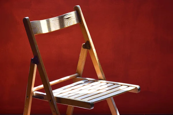 一张用木头做的空的旧折叠椅矗立在红漆墙前 在光影中嬉戏 — 图库照片