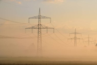 Sonbaharda sabah güneş yüksek elektrik direklerinin ardından yükselir, sislerin önünde ve Almanya 'da kızıl bir gökyüzü
