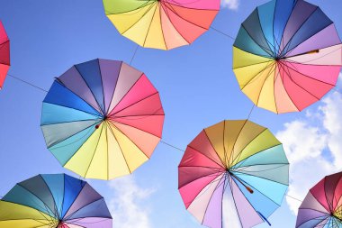 Gökkuşağının renklerinde renkli şemsiyeler mavi gökyüzüne karşı havada yan yana asılı duruyor.