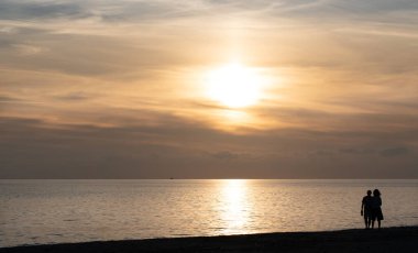 Bir adam ve bir kadın denizin kıyısında birlikte gün batımını izliyorlar. İkisinin de elinde cep telefonu var. Güneş bulutların ardında batıyor, kırmızı ışık yayıyor..