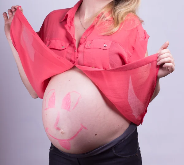 Hamile kızın göbek üzerinde mutlu gülen yüz boyalı — Stok fotoğraf