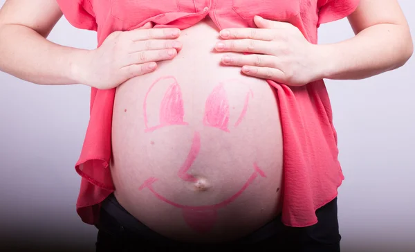 Раскрашенное счастливое смайлик на животе беременной девушки — стоковое фото