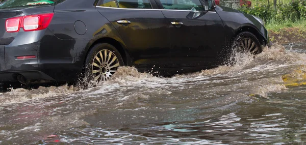 在后场大雨造成洪水期间被水淹没的道路上行驶的汽车 — 图库照片