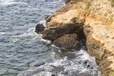 Deniz dalgaları su sıçramalarıyla kayalara çarpıyor.