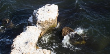 Deniz dalgaları su sıçramalarıyla kayalara çarpıyor.