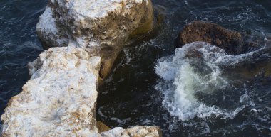 Deniz dalgaları su sıçramalarıyla kayalara çarpıyor..