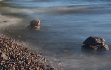 Deniz dalgaları plajda kayaya çarpıyor.