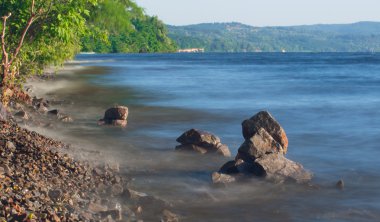 Deniz dalgaları plajda kayaya çarpıyor.
