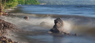 Deniz dalgaları plajda kayaya çarpıyor.