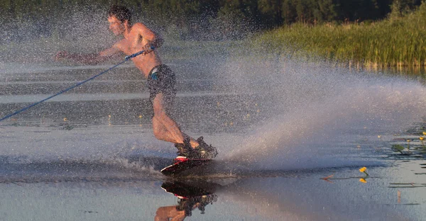 Wakeboarder athlete glides through the water with burning spray — Stock Photo, Image
