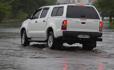 Şiddetli yağmurda sel basmış bir yolda araba sürüyor.