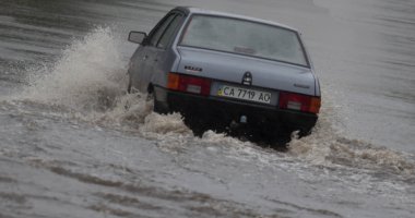 Şiddetli yağmurda sel basmış bir yolda araba sürüyor.