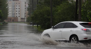 Şiddetli yağmurda sel basmış bir yolda araba sürüyor.