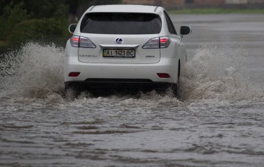Şiddetli yağmurda sel basmış bir yolda araba sürüyor.