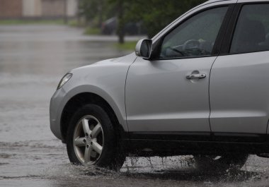 Şiddetli yağmurda sel basmış bir yolda araba sürüyor.