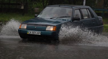 Şiddetli yağmurda sel basmış bir yolda araba sürüyor.