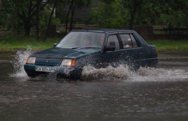 Şiddetli yağmurda sel basmış bir yolda araba sürüyor.
