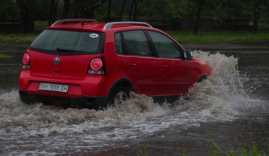 Şiddetli yağmurda sel basmış bir yolda araba sürüyor.