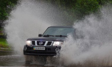 Şiddetli yağmurda sel basmış bir yolda araba sürüyor.
