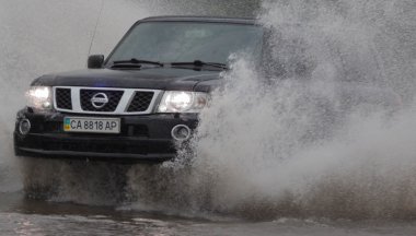 Şiddetli yağmurda sel basmış bir yolda araba sürüyor.