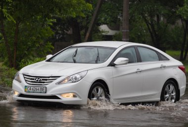 Şiddetli yağmurda sel basmış bir yolda araba sürüyor.