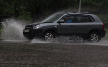 Şiddetli yağmurda sel basmış bir yolda araba sürüyor.