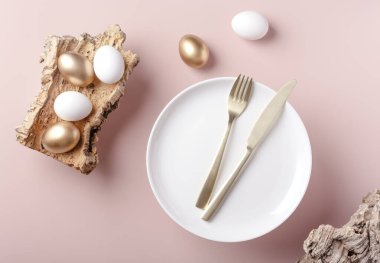 Paskalya beyaz ve altın yumurtaları bir ağacın kabuğunda, çatal bıçak takımlı bir tabağın yanında, tozlu arka plan, yatay yönelim