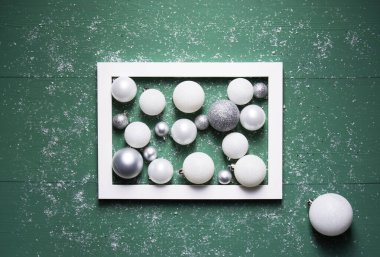 Noel kompozisyonu beyaz ve gri toplar karla kaplı yeşil ahşap bir zeminde beyaz bir çerçeve içinde yatar. Yakın plan, yatay yönelim