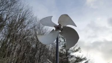 Rüzgâr değirmeni bir kış günü rüzgarda yavaşça dönüyor. Arkasında bulutlar ve ormanlar var. 