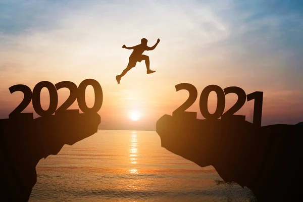 Mutlu yıllar 2021 ve siluet konsepti 2020 'den 2021' e güzel turuncu gökyüzü ve deniz ile atlayan adam..