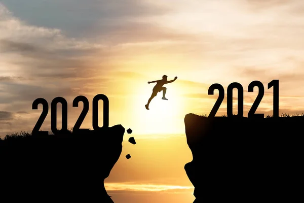 Mutlu Noeller ve mutlu yıllar 2021, Siluet Adam 2020 uçurumundan 2021 uçurumuna bulutlu gökyüzü ve güneş ışığıyla atlayan.