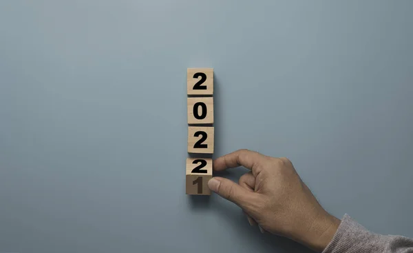 ブルーの背景に2021年から2022年に変更する木製ブロックキューブを反転手 メリークリスマスと幸せな新年の準備コンセプト — ストック写真