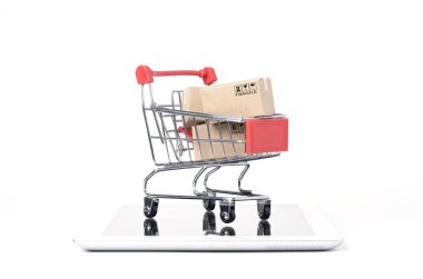 Kırmızı alışveriş arabasının içinde beyaz arka plan ve fotokopi alanı, çevrimiçi alışveriş ve e-ticaret konsepti olan tablet üzerindeki kargo kutularından izole edilmiş..