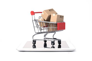 Kırmızı alışveriş arabasının içinde beyaz arka plan ve fotokopi alanı, çevrimiçi alışveriş ve e-ticaret konsepti olan tablet üzerindeki kargo kutularından izole edilmiş..