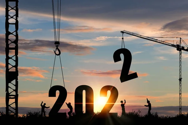 2022 yılbaşı partisi hazırlıkları için gökyüzü bulutlu ve vinçli inşaat işçisi silueti..